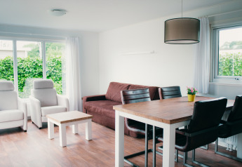 Salon moderne à la Veluwelodge au parc De Boshoek, Pays-Bas, avec mobilier clair et grandes fenêtres.