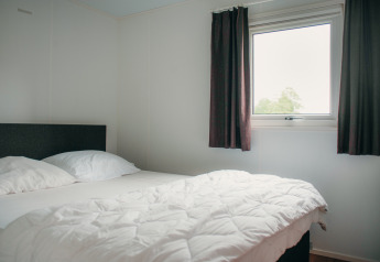 Slaapkamer in Veluwelodge op vakantiepark De Boshoek, Nederland, met bed, raam en donkere gordijnen.