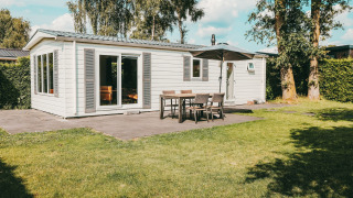 Vista esterna della Veluwe lodge con patio, tavolo e ombrellone al Holiday park De Boshoek nei Paesi Bassi.