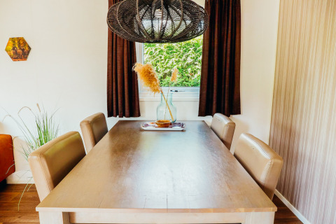 Bright dining area in Veluwe Lodge with wooden table, four chairs, and window view at De Boshoek, Netherlands.