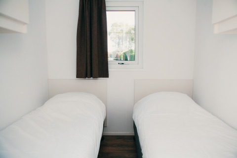 Zwei Einzelbetten in einem hellen, minimalistischen Raum mit Fenster im Veluwe Lodge + Sauna, Niederlande.