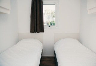 Dos camas individuales en una habitación minimalista y luminosa con ventana en Veluwe lodge + sauna, Holanda.