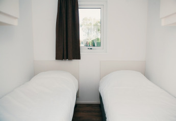 Twee eenpersoonsbedden in een lichte, minimalistische kamer met raam in Veluwe lodge + sauna, De Boshoek.