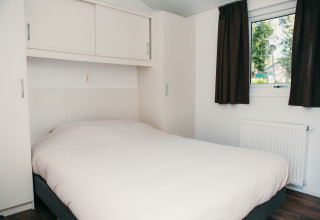 Schlafzimmer mit Doppelbett, weißen Schränken und Fenster in der Veluwe lodge + sauna, Ferienpark De Boshoek.