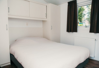 Bedroom with double bed, white cabinets, curtains and window at Veluwe lodge + sauna, Holiday park De Boshoek, Netherlands.