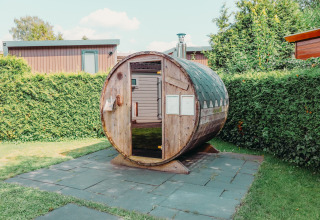 Outdoor barrel sauna next to a Veluwe lodge at Holiday park De Boshoek in the Netherlands, with hedges.