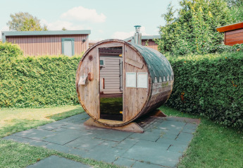 Buitensauna in de vorm van een ton bij een Veluwe lodge op Holiday park De Boshoek, omgeven door hagen.