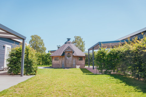Foto af en træhytte og grønne omgivelser på Veluwelodge XL, feriepark De Boshoek, Holland.