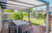 Covered patio with dining table and chairs at Veluwelodge XL, Holiday park De Boshoek, Netherlands, sunny day.