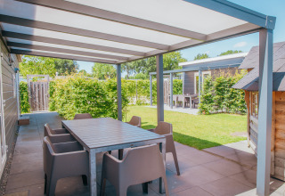 Udendørs terrasse med spisebord og stole ved Veluwelodge XL, feriepark De Boshoek, Holland, solskinsdag.