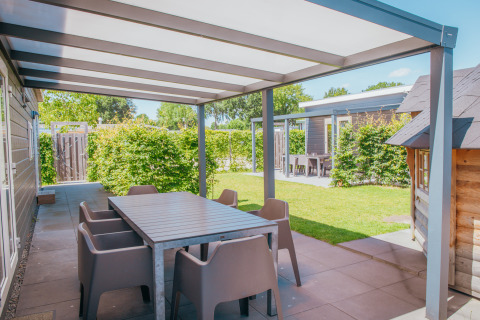 Udendørs terrasse med spisebord og stole ved Veluwelodge XL, feriepark De Boshoek, Holland, solskinsdag.