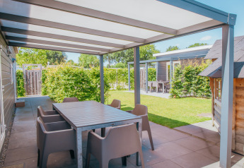 Terraza cubierta con mesa y sillas en Veluwelodge XL, parque vacacional De Boshoek, Países Bajos, día soleado.