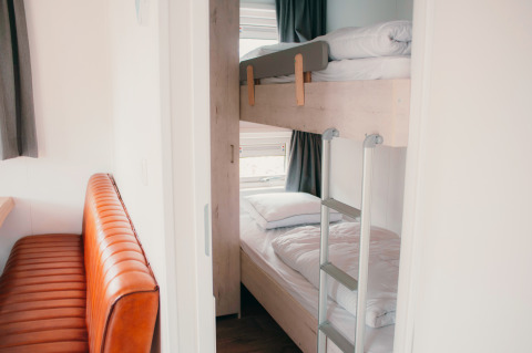 Binnenzicht van Veluwelodge XL op vakantiepark De Boshoek, met stapelbedden en een lederen zitbank.