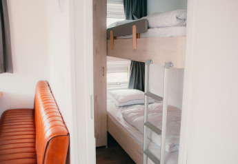 Binnenzicht van Veluwelodge XL op vakantiepark De Boshoek, met stapelbedden en een lederen zitbank.