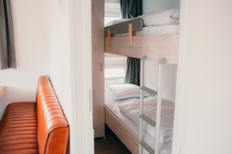 Vista interior de Veluwelodge XL en Holiday park De Boshoek, con literas y banco de cuero.