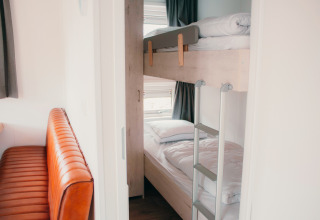 Interieur van Veluwelodge XL bij vakantiepark De Boshoek, met stapelbedden en een leren bank.