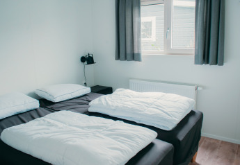 Soveværelse i Veluwelodge XL på Holiday park De Boshoek, Nederlandene med to enkeltsenge og lyst interiør.