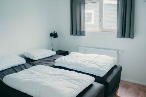 Soveværelse i Veluwelodge XL på Holiday park De Boshoek, Nederlandene med to enkeltsenge og lyst interiør.