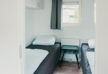 Habitación con dos camas individuales, ventana y mesa pequeña en Veluwelodge XL, De Boshoek Holiday Park, Países Bajos.