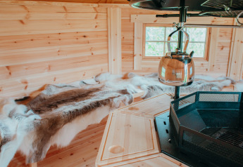 Interno della Veluwelodge XL con pareti in legno, pelli di renna e bollitore su camino a De Boshoek.