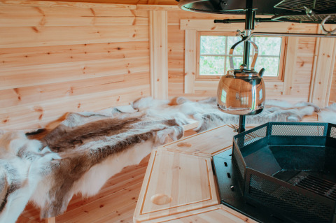 Interior of Veluwelodge XL with wooden walls, reindeer hides and kettle on fireplace at De Boshoek, Netherlands.