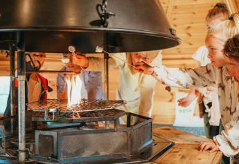 Niños asan malvaviscos al fuego en la Veluwelodge XL del parque vacacional De Boshoek, Países Bajos.