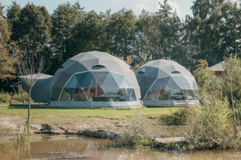 Dos tiendas redondas de glamping junto a un estanque en Holiday Park Sallandshoeve, Países Bajos, rodeadas de naturaleza.
