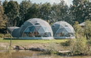 To runde glampingtelte på plænen ved vandkanten i Holiday Park Sallandshoeve, Holland, omgivet af natur.