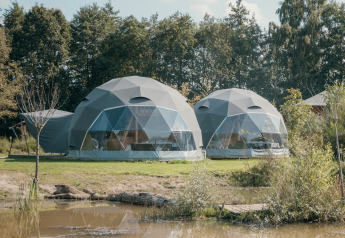 To runde glampingtelte på plænen ved vandkanten i Holiday Park Sallandshoeve, Holland, omgivet af natur.