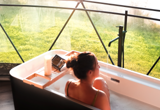 Femme se relaxant dans une baignoire avec vue sur la nature au Round Holly Tent, Holiday Park Sallandshoeve, Pays-Bas.
