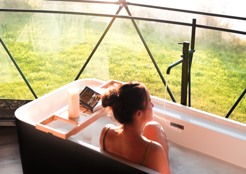 Femme se relaxant dans une baignoire avec vue sur la nature au Round Holly Tent, Holiday Park Sallandshoeve, Pays-Bas.
