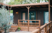 Luxe lodge met houten veranda en omheining, omringd door bomen en een rustige, groene omgeving.