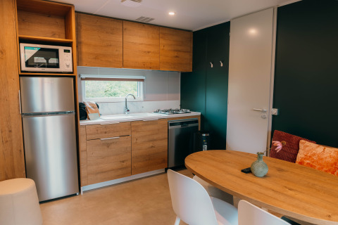 Cocina moderna en Luxury Lodge con muebles de madera, mesa de comedor, sillas blancas, nevera y ventana.
