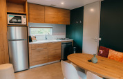 Moderne køkken i Luxury Lodge med træskabe, spisebord, hvide stole, køleskab og vindue med udsigt.