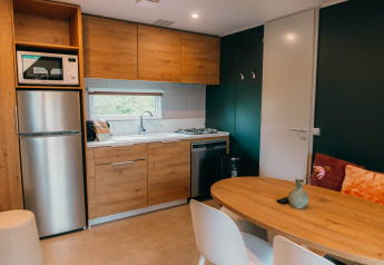 Cocina moderna en Luxury Lodge con muebles de madera, mesa de comedor, sillas blancas, nevera y ventana.