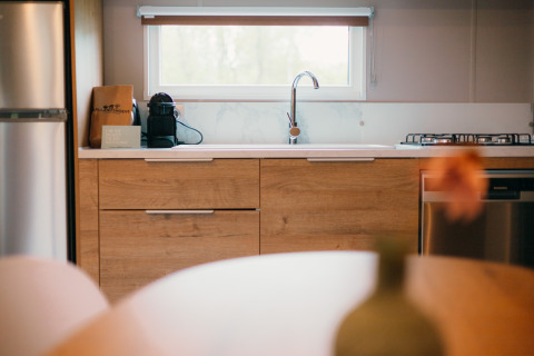 Moderne Küche in der Luxury Lodge mit Holzschränken, Kaffeemaschine, Gasherd und großem Fenster.