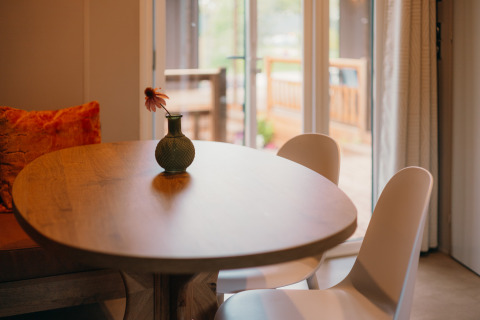 Round wooden table with a vase and flower, two chairs, and patio view inside Luxury Lodge.