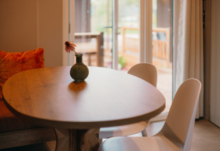 Ronde houten tafel met vaas en bloem, twee stoelen en uitzicht op terras in Luxury Lodge.