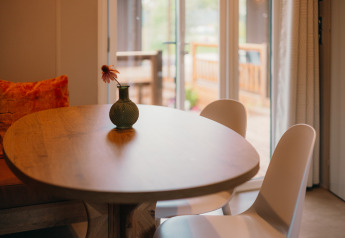 Ronde houten tafel met vaas en bloem, twee stoelen en uitzicht op terras in Luxury Lodge.