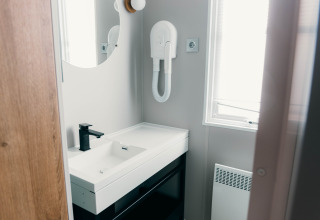 Modernes Badezimmer im Luxury Lodge mit schwarzem Wasserhahn, Spiegel, Föhn und Fenster mit Tageslicht.