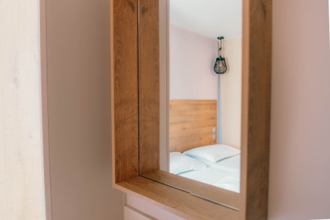 Reflet dans le miroir d’un lit moderne à tête en bois et lampe design dans une chambre Luxury Lodge.