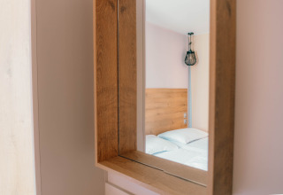 Reflet dans le miroir d’un lit moderne à tête en bois et lampe design dans une chambre Luxury Lodge.