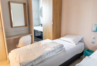 Habitación luminosa en Luxury Lodge con cama individual, escritorio, espejo y acceso a baño moderno.