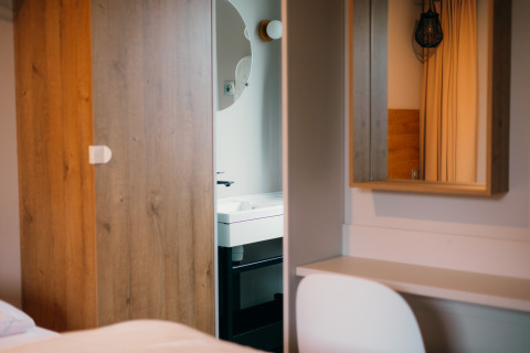 Chambre moderne à Luxury Lodge avec armoire en bois, bureau, miroir mural et vue sur la salle de bain.