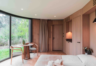 Vista interior de la tiny house Lumni Pod en Wilsumer Berge, Alemania, con madera y grandes ventanales.
