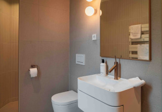 Baño moderno en Lumni Pod en Wilsumer Berge, Alemania, con inodoro, lavabo y espejo iluminado.
