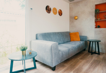 Modern living room in Family Lodge at Holiday park De Boshoek, Netherlands, with grey sofa and orange pillow.