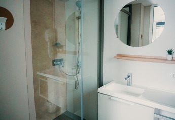Baño moderno con ducha, espejo redondo, lavabo y planta en Family Lodge, Holiday park De Boshoek, Países Bajos.