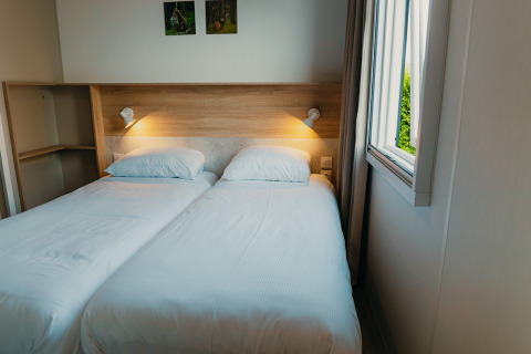 Zwei Einzelbetten mit weißer Bettwäsche in einem Zimmer der Family Lodge im Ferienpark De Boshoek, Niederlande.