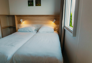 Zwei Einzelbetten mit weißer Bettwäsche in einem Zimmer der Family Lodge im Ferienpark De Boshoek, Niederlande.
